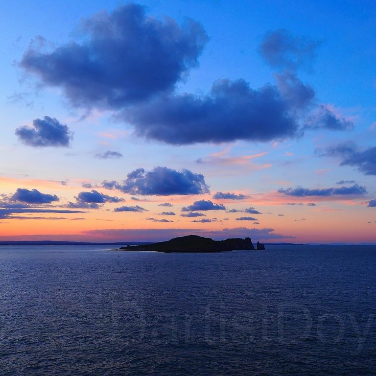 Un paysage marin au coucher du soleil, avec la silhouette d'une île sous un ciel nuageux.