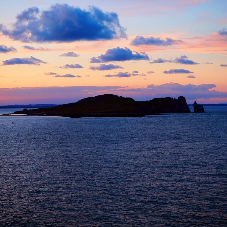 Un paysage marin au coucher du soleil, avec la silhouette d'une île sous un ciel nuageux.