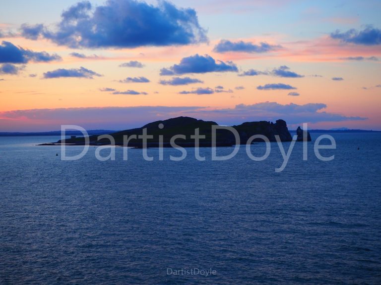 Silhouette d'une île contre un ciel coloré au coucher du soleil sur l'eau.