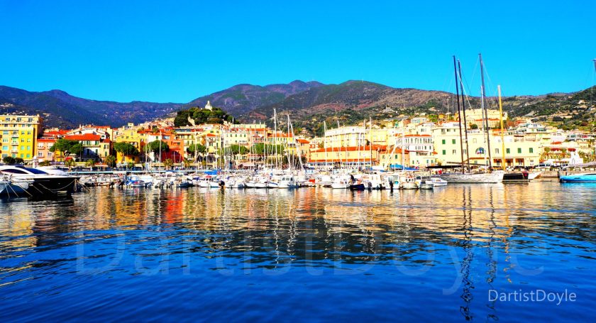 Vue du port avec des bateaux et des bâtiments colorés, sous un ciel bleu.