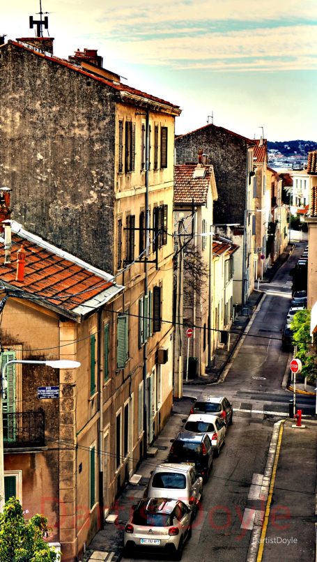 Rue étroite bordée de bâtiments anciens et de voitures stationnées.