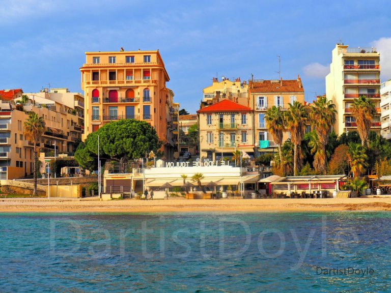 Vue d'un bord de mer avec des bâtiments colorés et des palmiers.